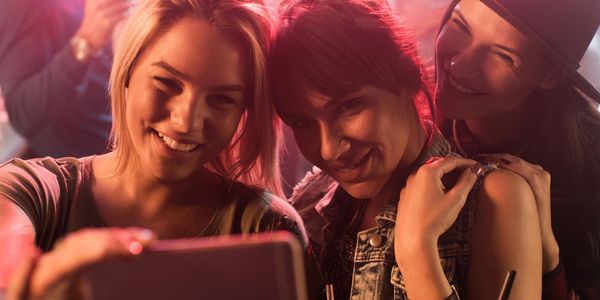 Three friends happily taking a selfie together in a warmly lit setting.