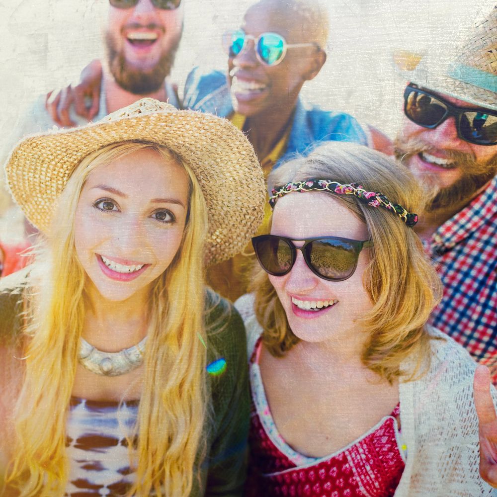 Five friends smiling and enjoying a sunny day outdoors, wearing sunglasses and hats.