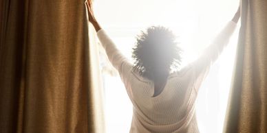 Person opening curtains to bright morning light.