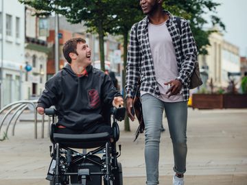 Two friends happily walking and talking, one in a wheelchair.