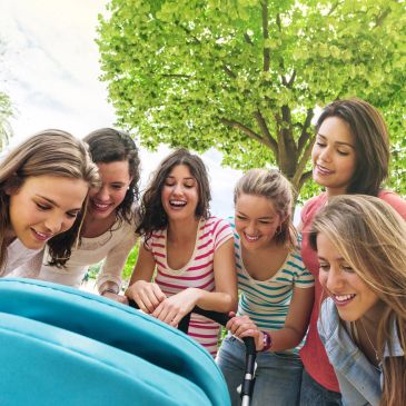 Group of women happily looking at a baby stroller outdoors.
