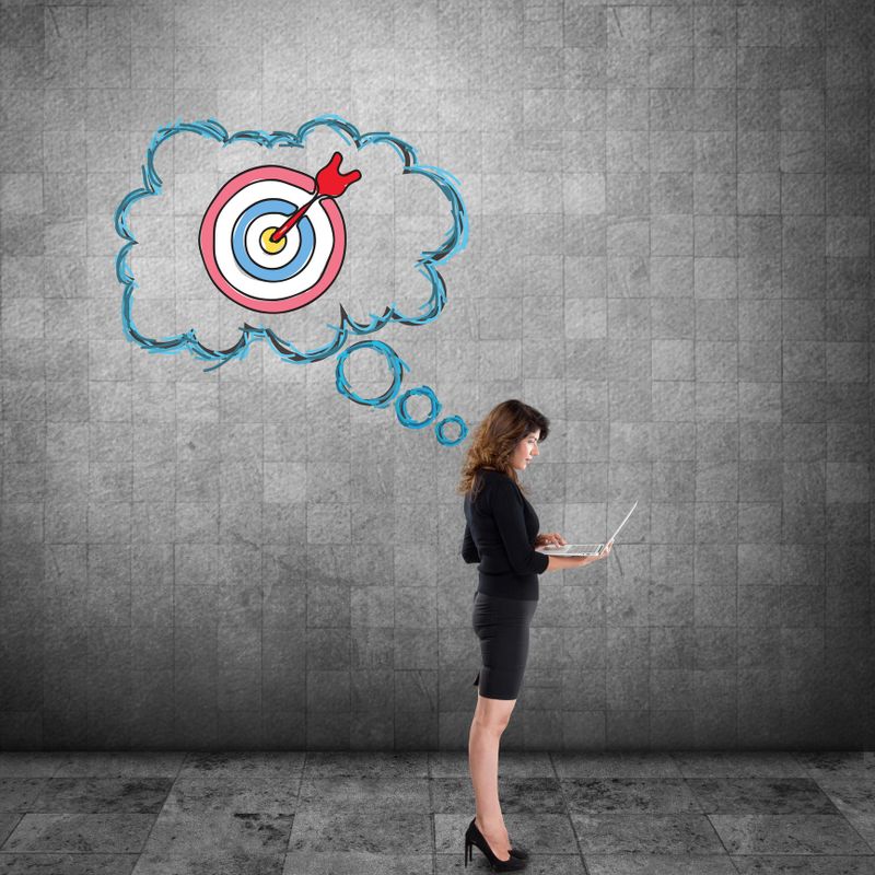 Successful young businesswoman working on laptop and bull's eye target drawn on wall as concept of winner.