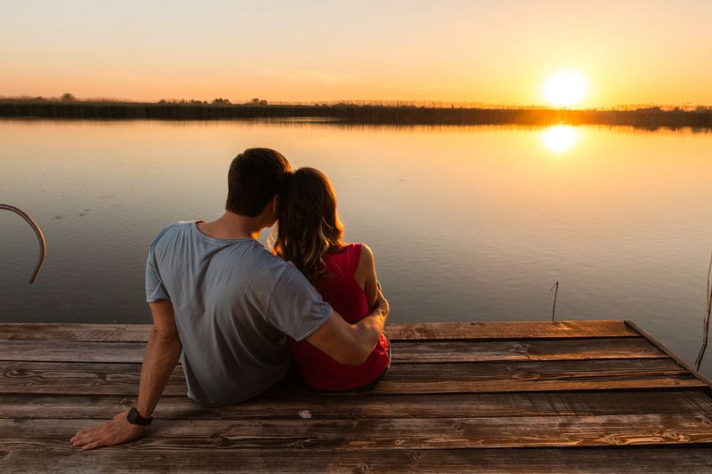 Rear view of romantic couple enjoying the view on a pier at sunset.
