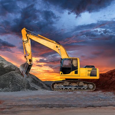 Yellow excavator digging gravel at sunset under dramatic skies.