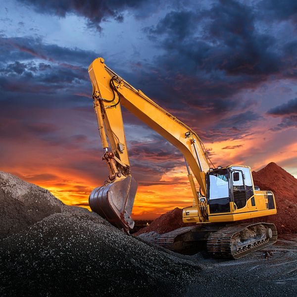 Yellow excavator working on a gravel pile at sunset.