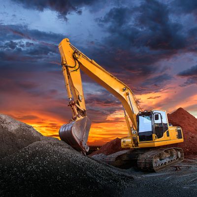 Yellow excavator working on gravel piles during a vivid sunset.