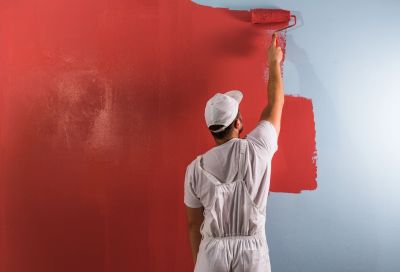 Painter rolling red paint over a blue wall.