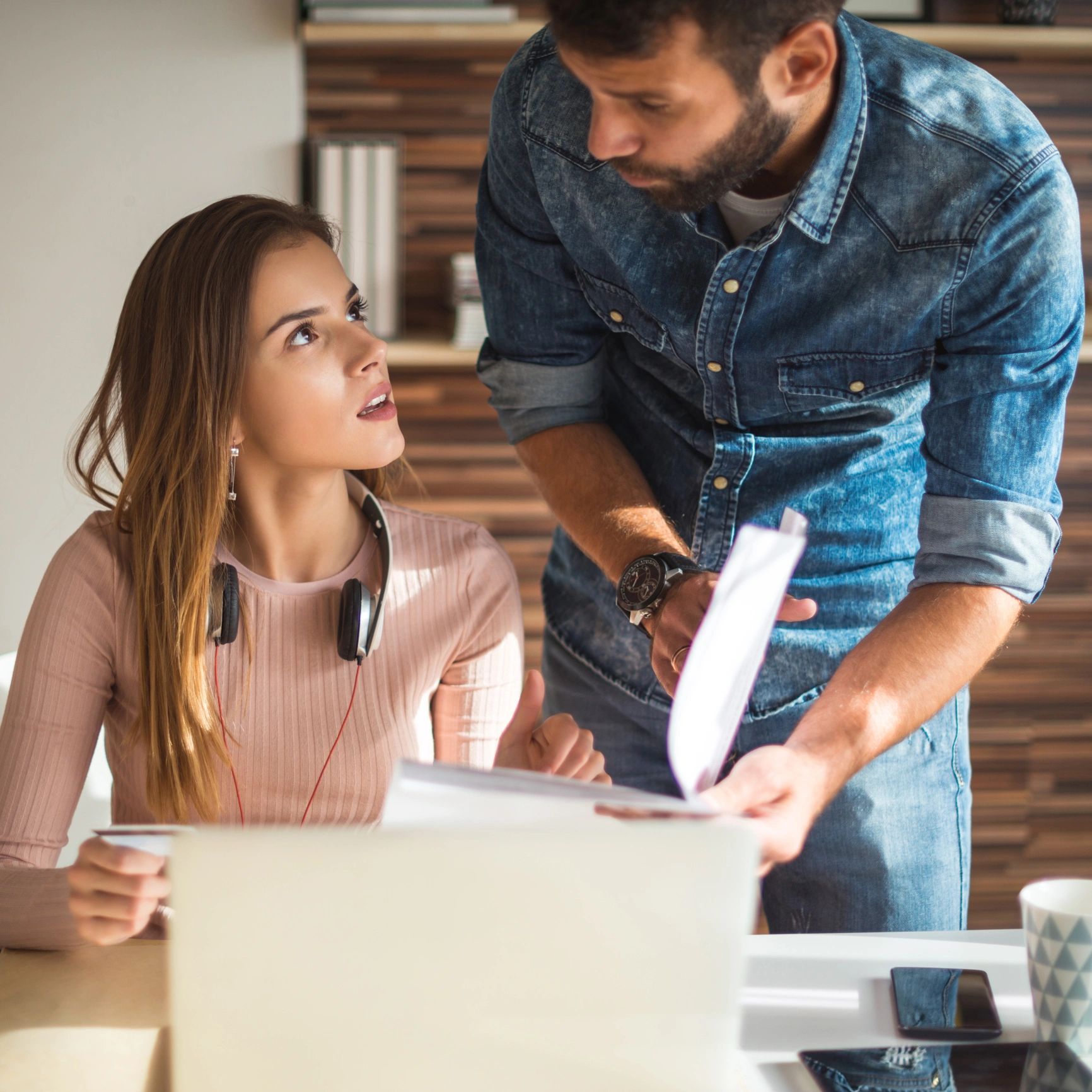 Man and woman discussing documents at a desk in a casual office setting.