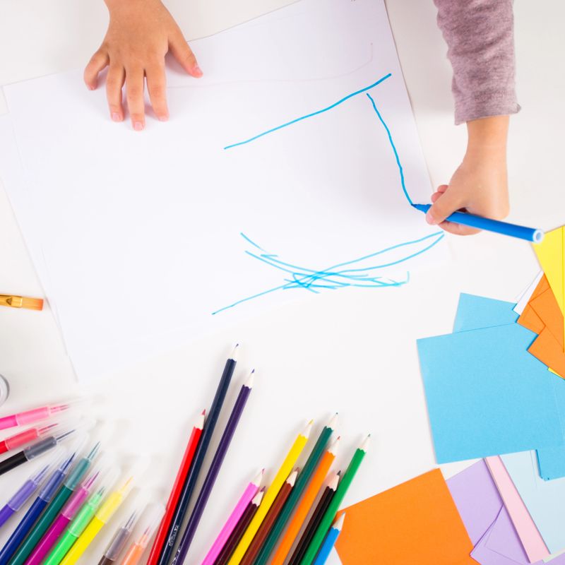 little girl drawing with colored pencils on paper
