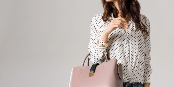 Woman in polka dot blouse holding a pink handbag.