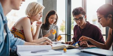 A group of diverse young adults studying together around a table with books and notes.