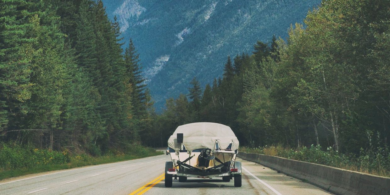 Boat being towed on a mountain highway surrounded by trees.