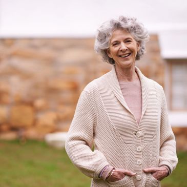 Smiling elderly woman in a cozy beige cardigan outdoors.