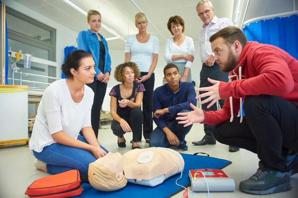 Group learning CPR with instructor and mannequin on floor.