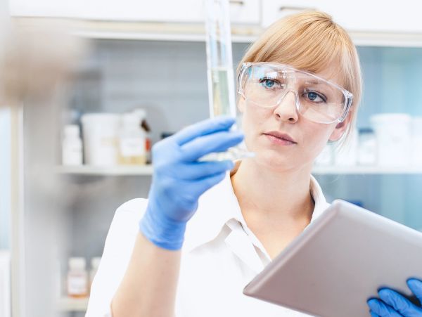 Scientist examining a test tube in a laboratory while holding a tablet.