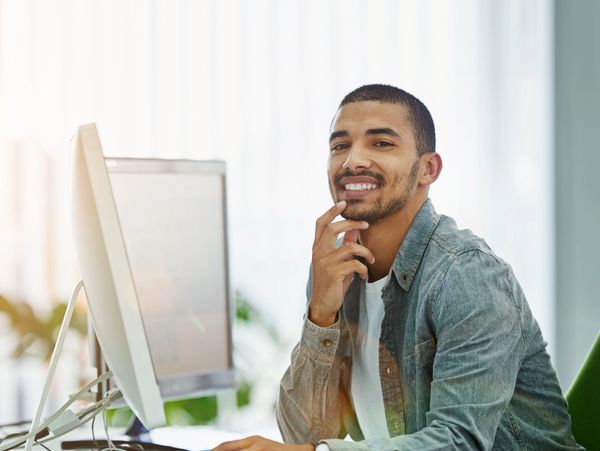 Man smiling while working on a computer in a bright office.