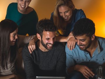 A group of friends happily watching something on a tablet together.