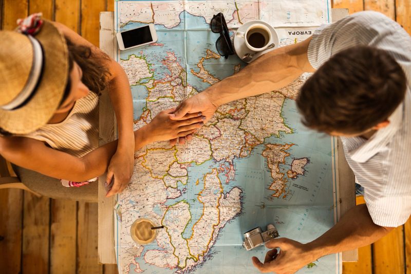 High angle view of a couple holding hands and choosing where to travel while examining a map.