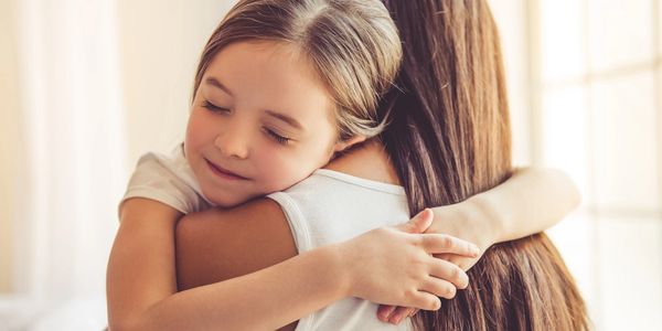 A young girl warmly hugging an adult with closed eyes, expressing affection.