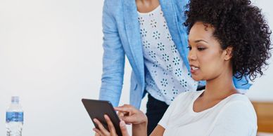 Two women engaged with a tablet, collaborating in a bright office.