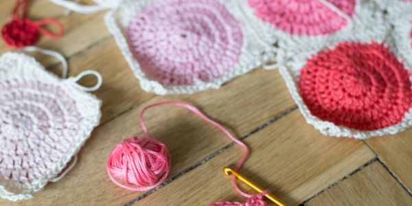Crochet squares with pink yarn and a crochet hook on a wooden surface.
