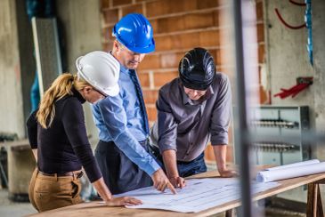 Three engineers reviewing blueprints on site.