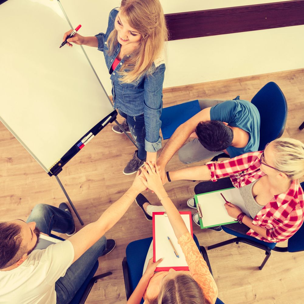 Group of young people joining hands in teamwork during a meeting.