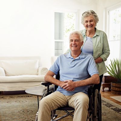 Smiling elderly man in wheelchair with a happy woman standing behind him.