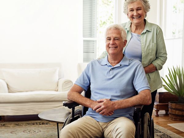 An elderly man in a wheelchair with a smiling elderly woman standing behind him.
