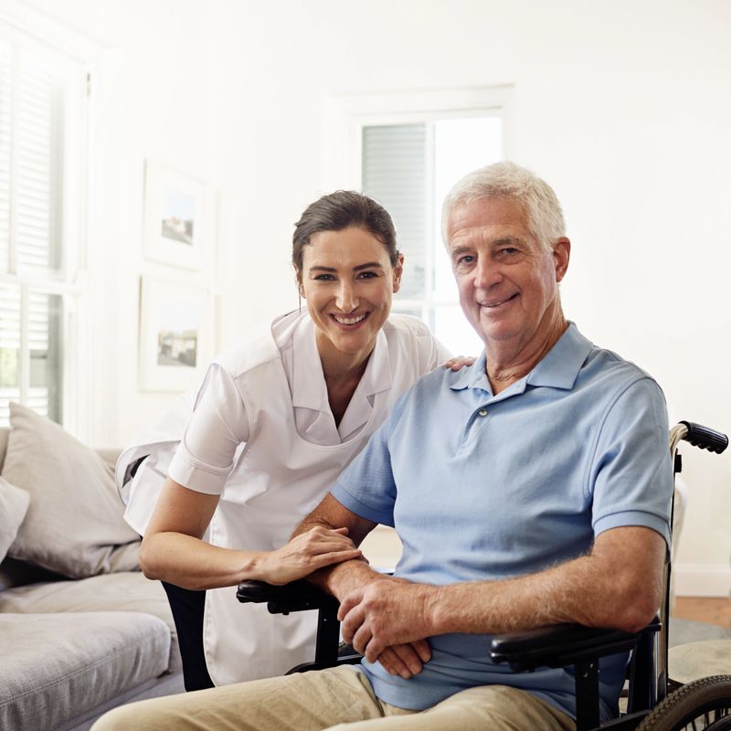Portrait of a smiling caregiver and a senior man in a wheelchair at home