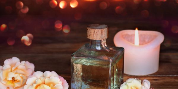 A lit candle, perfume bottle, and soft flowers create a cozy, warm ambiance.
