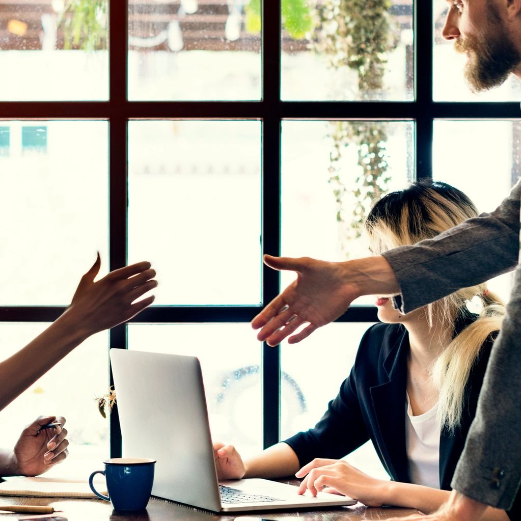 People in a business meeting reaching out for a handshake near a laptop.