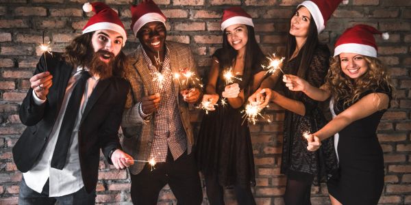 Group of friends with sparklers and Santa hats celebrating.