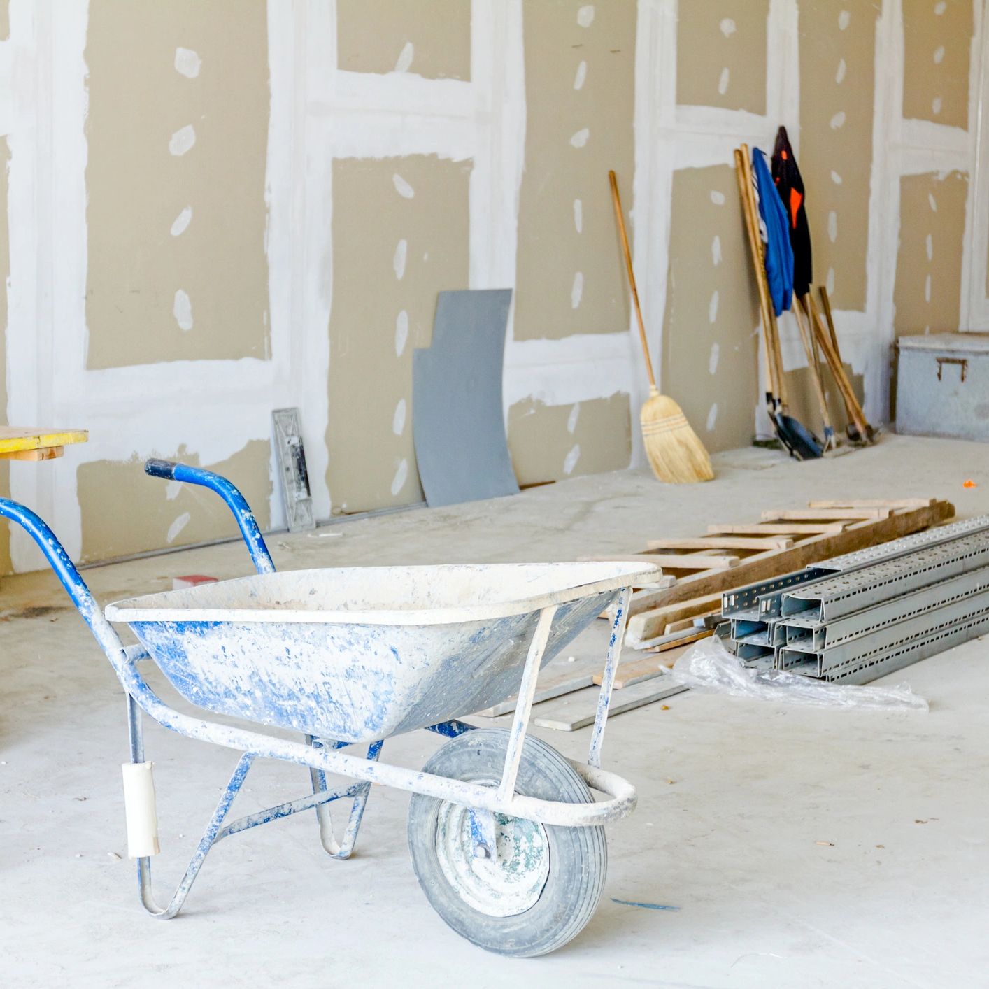 A wheelbarrow in an unfinished construction area with tools and materials.