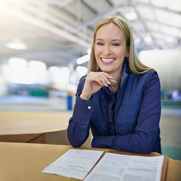 Smiling woman in a blue vest working with documents in a warehouse.