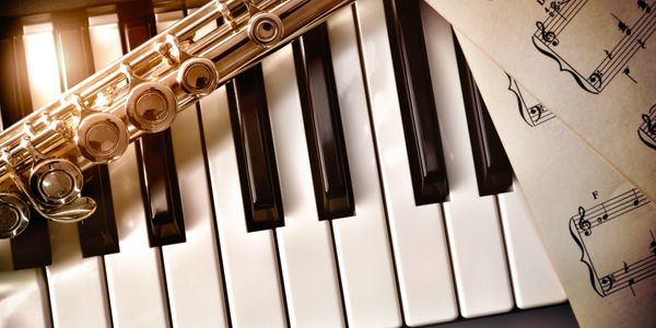 Flute resting on piano keys with sheet music.