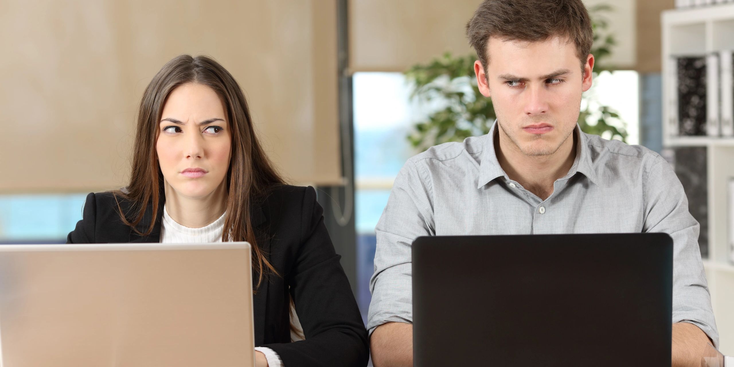 Man and woman looking suspiciously at each other at work.