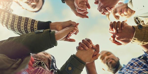 Group of diverse people standing in a circle holding hands against the sky.