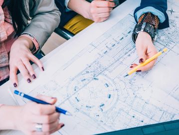 Two people collaborating on architectural blueprints with pens.