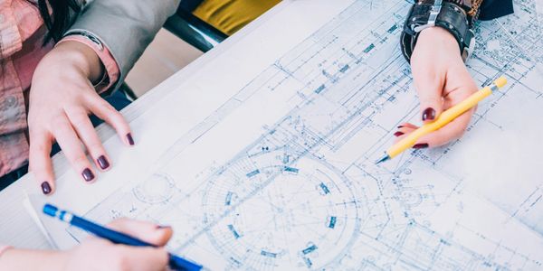 Two people working on architectural blueprints with pencils.
