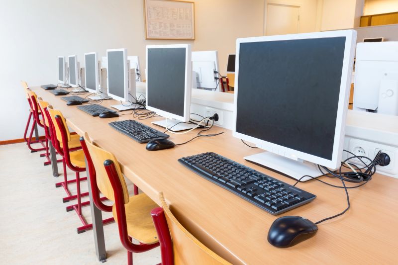 Computer education in classroom on high school. On this long table you see many desktop computers with keyboards and computer mouses. Also many chairs for the children to sit and work with the computer. In this classroom the students get computer lessons so they get prepared for our digital society as a lifestyle