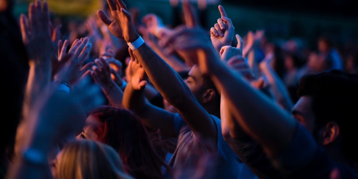 Crowd raising hands at a lively event with blue and orange lighting.