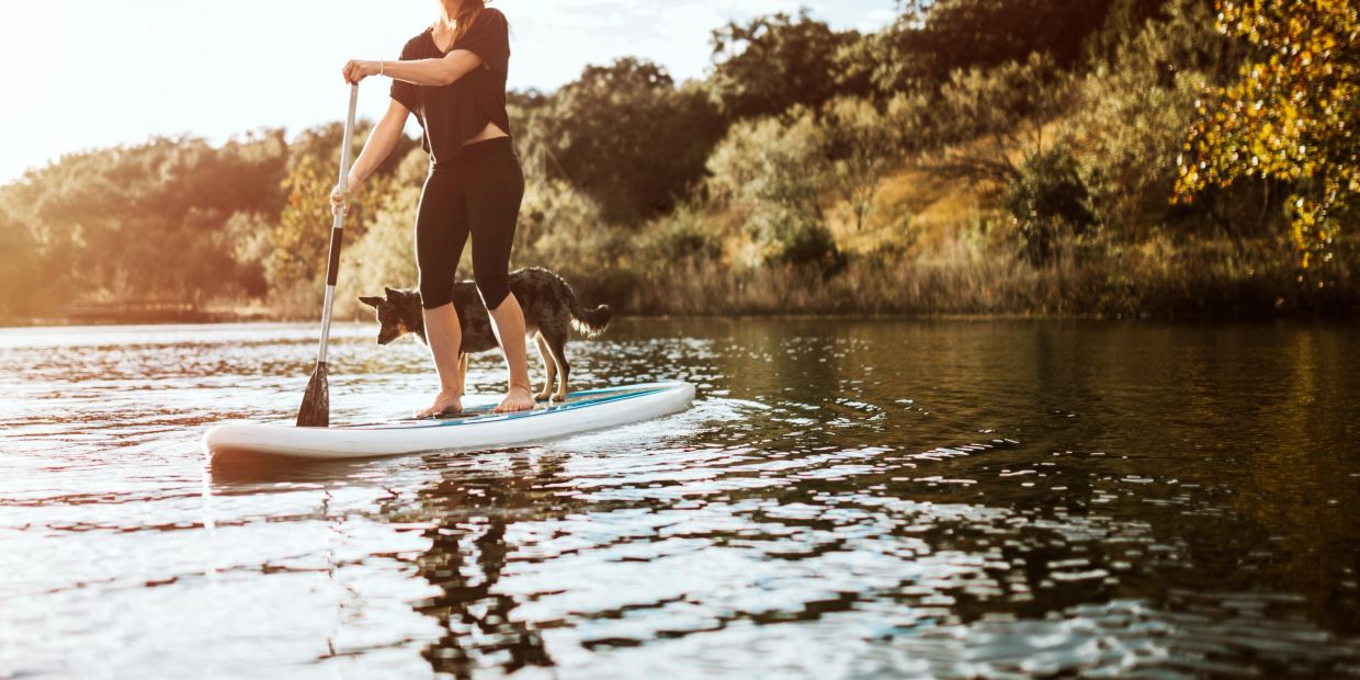 Woman paddleboarding with her dog on a calm lake.