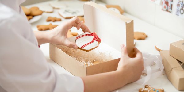 Person packing decorated Christmas cookies in a gift box.