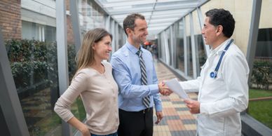 Couple shaking hands with a doctor in a hospital corridor.