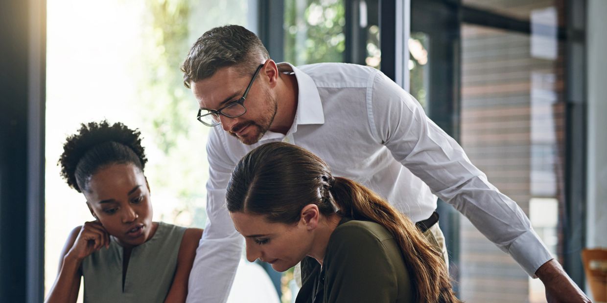 Three colleagues engaged in a focused discussion around a table in a modern office.