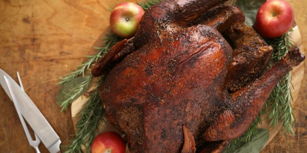 Cooked turkey with apples and rosemary on a wooden board.