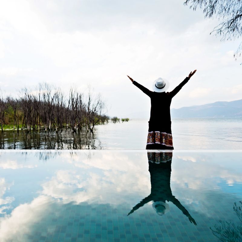Young woman standing at bay of water with arms raised.