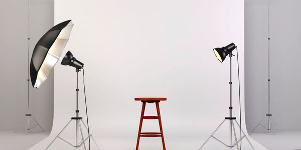Photo studio setup with stool and lighting equipment against a white backdrop.