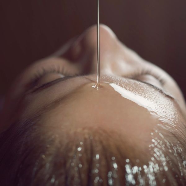 Close-up of oil being poured on a person's forehead during a skincare treatment.